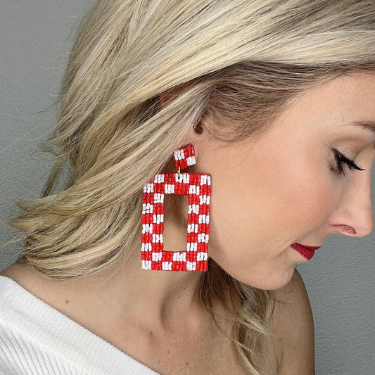 A person wearing oversized red and white checkered beaded earrings.