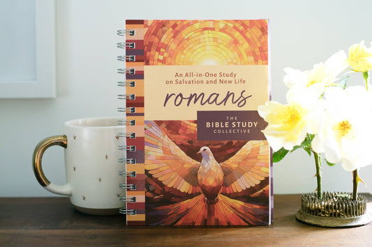 Notebook titled 'Romans' by The Bible Study Collective on a table with a mug and flowers.