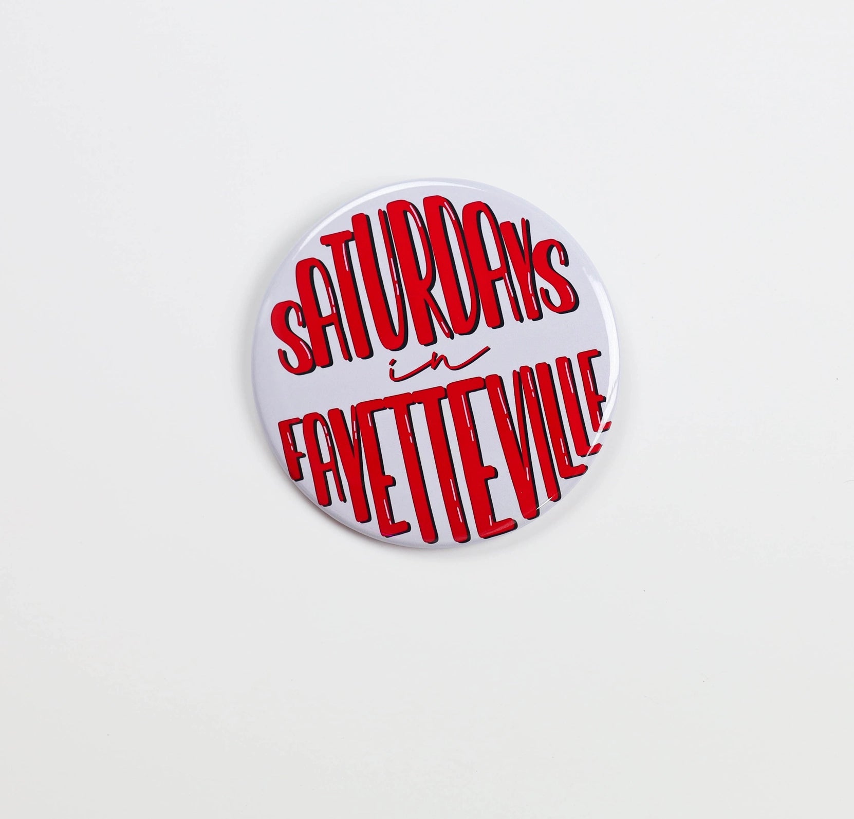 Button and gameday pin with 'Saturdays in Fayetteville' text in red on a white background, Razorback gameday pins, Arkansas gameday pins, Saturdays in Fayetteville gameday pin, Saturdays in Fayetteville gameday button, shopping in Fayetteville ar