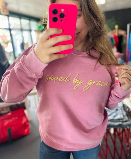 Person wearing a pink sweatshirt with 'saved by grace' text, holding a pink phone case.