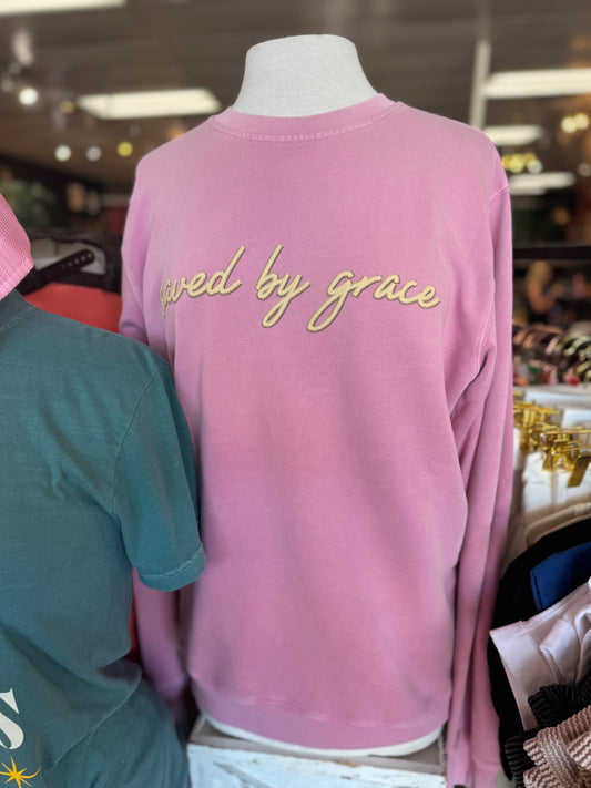 Pink long-sleeve shirt with 'lived by grace' text on a mannequin in a store setting.