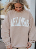 Load image into Gallery viewer, A woman wearing a beige ribbed crewneck sweatshirt with 'ARKANSAS' printed in large white block letters across the chest, from Whimsy Whoo boutique’s Razorback shop in Fayetteville.
