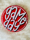Load image into Gallery viewer, Circular red sign with 'game day' text on a textured beige background
