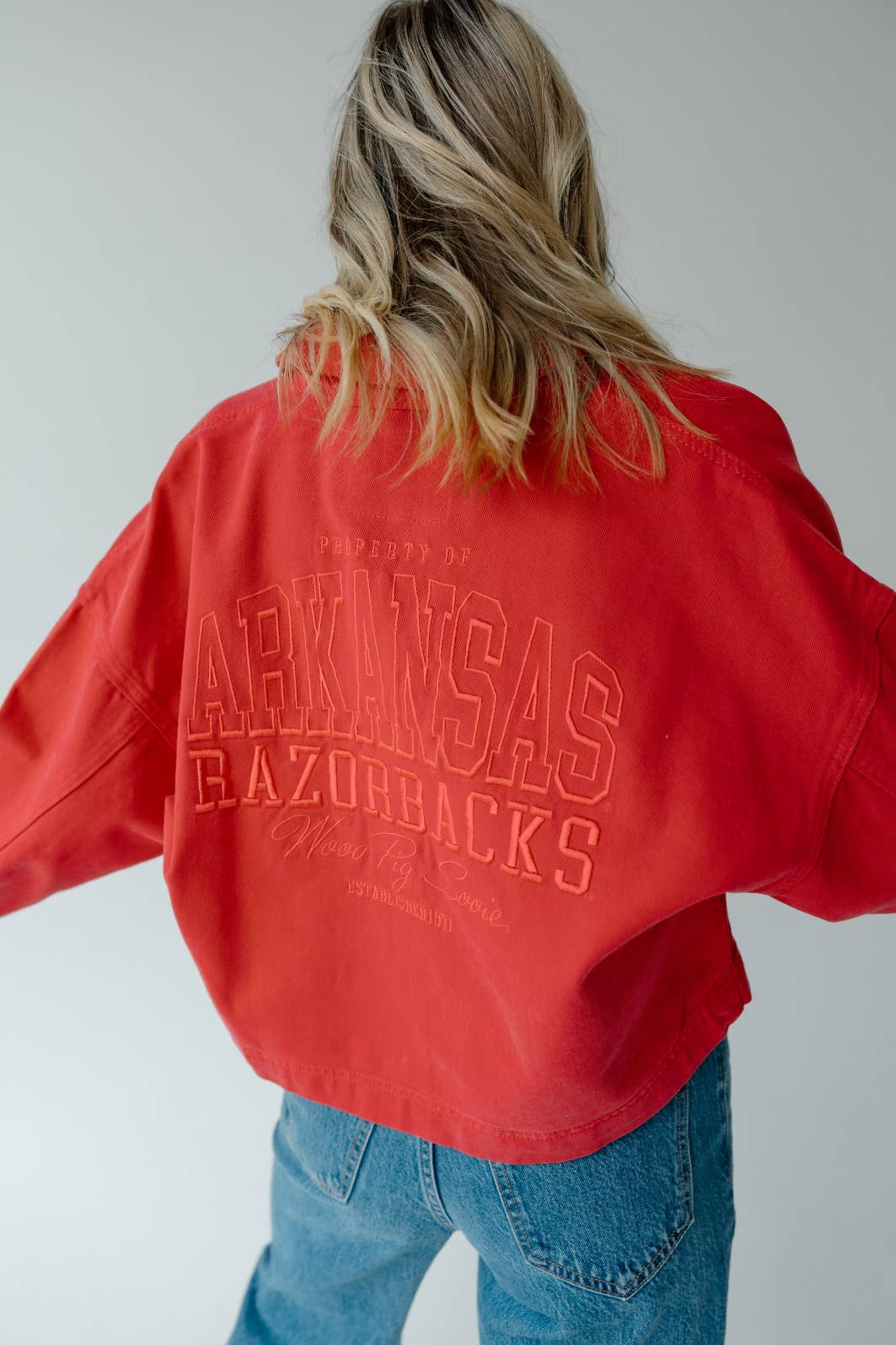 Person wearing a red 'ARKANSAS RAZORBACKS' jacket in a Fayetteville Arkansas razorback store, arknasas razorback red jacket, Arkansas razorback outerwear, arkansas razorback store, Fayetteville ar shopping