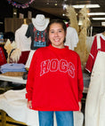 Load image into Gallery viewer, A smiling woman wearing a bright red sweatshirt with 'HOGS' in large white varsity-style letters across the chest, standing in a Fayetteville boutique retail store.
