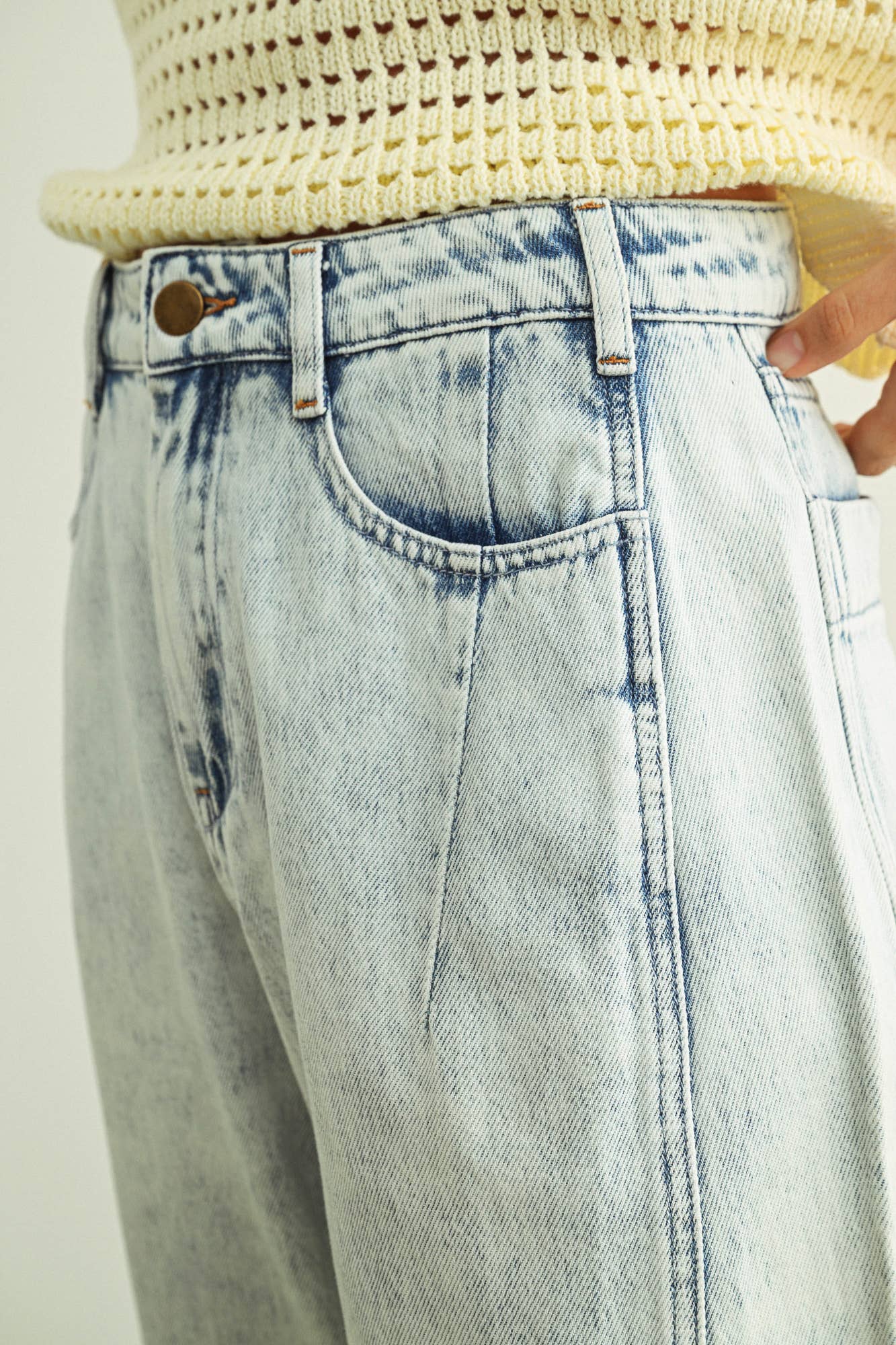 Light blue jeans with a beige knit top on a plain background