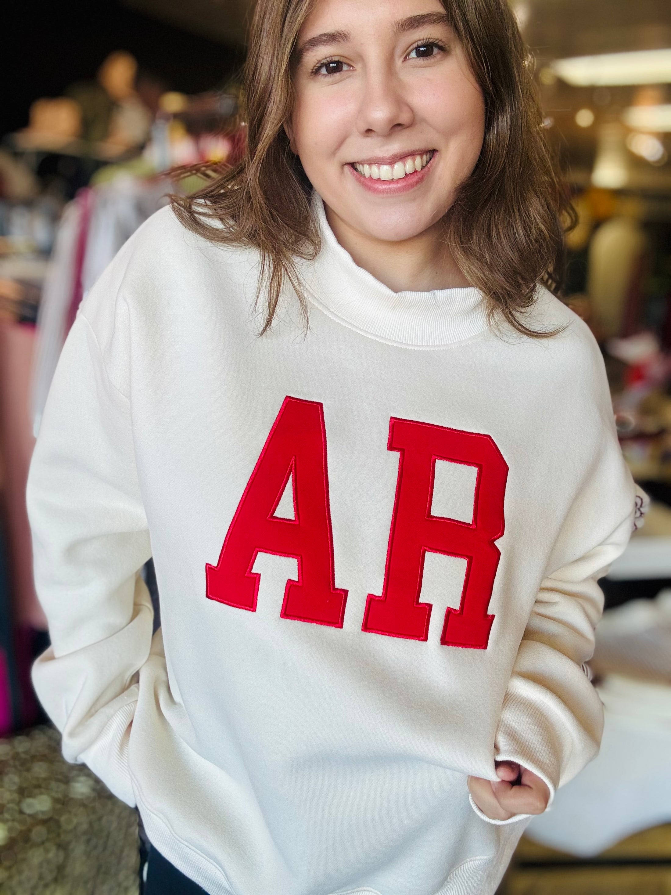 A mirror selfie of a model wearing the cream AR embroidered mock neck sweatshirt at Whimsy Store, a premier Arkansas Razorback store in Fayetteville AR.