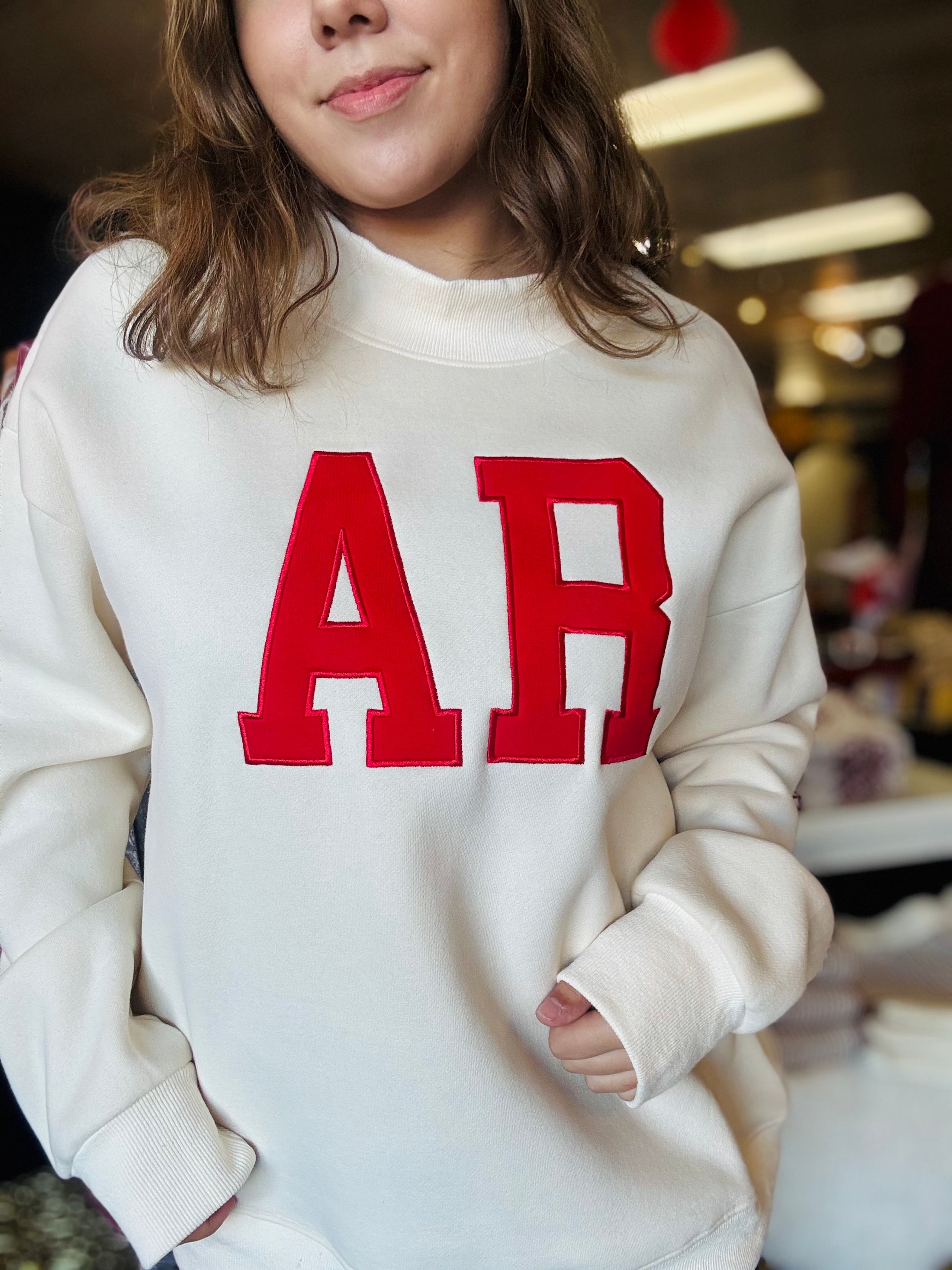 Close-up of the high-quality red AR embroidery on the cream mock neck sweatshirt, exclusive to Whimsy Store’s Razorback football store collection.