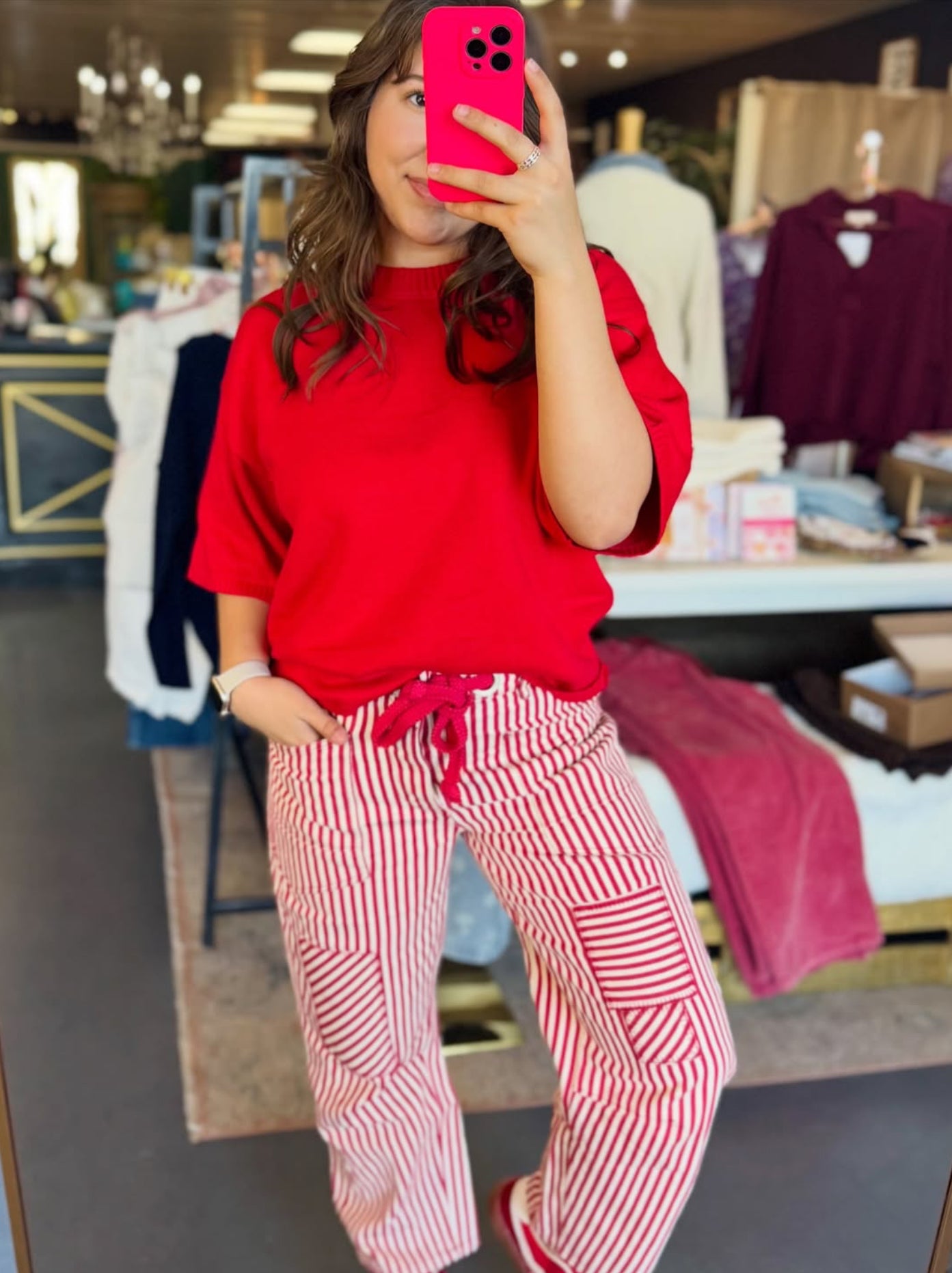 A mirror selfie showing a woman styling red and white striped barrel pants with a solid red top, creating a trendy boutique look for an Arkansas Hogs fan.