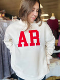 Load image into Gallery viewer, Model showcasing the oversized cream sweatshirt with red AR embroidery, perfect for gameday at a top boutique in Arkansas.
