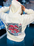 Load image into Gallery viewer, Woman wearing the Bloom Into Spring Arkansas Razorback hoodie in a Fayetteville boutique, styled for University of Arkansas football game day with oversized women’s Razorback apparel.

