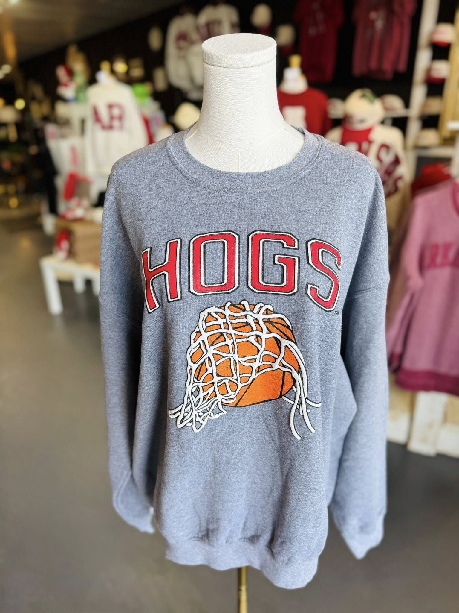 The Hogs Basketball grey crewneck sweatshirt displayed on a mannequin inside Whimsy Whoo Boutique, showing the relaxed fit and bold red graphic.