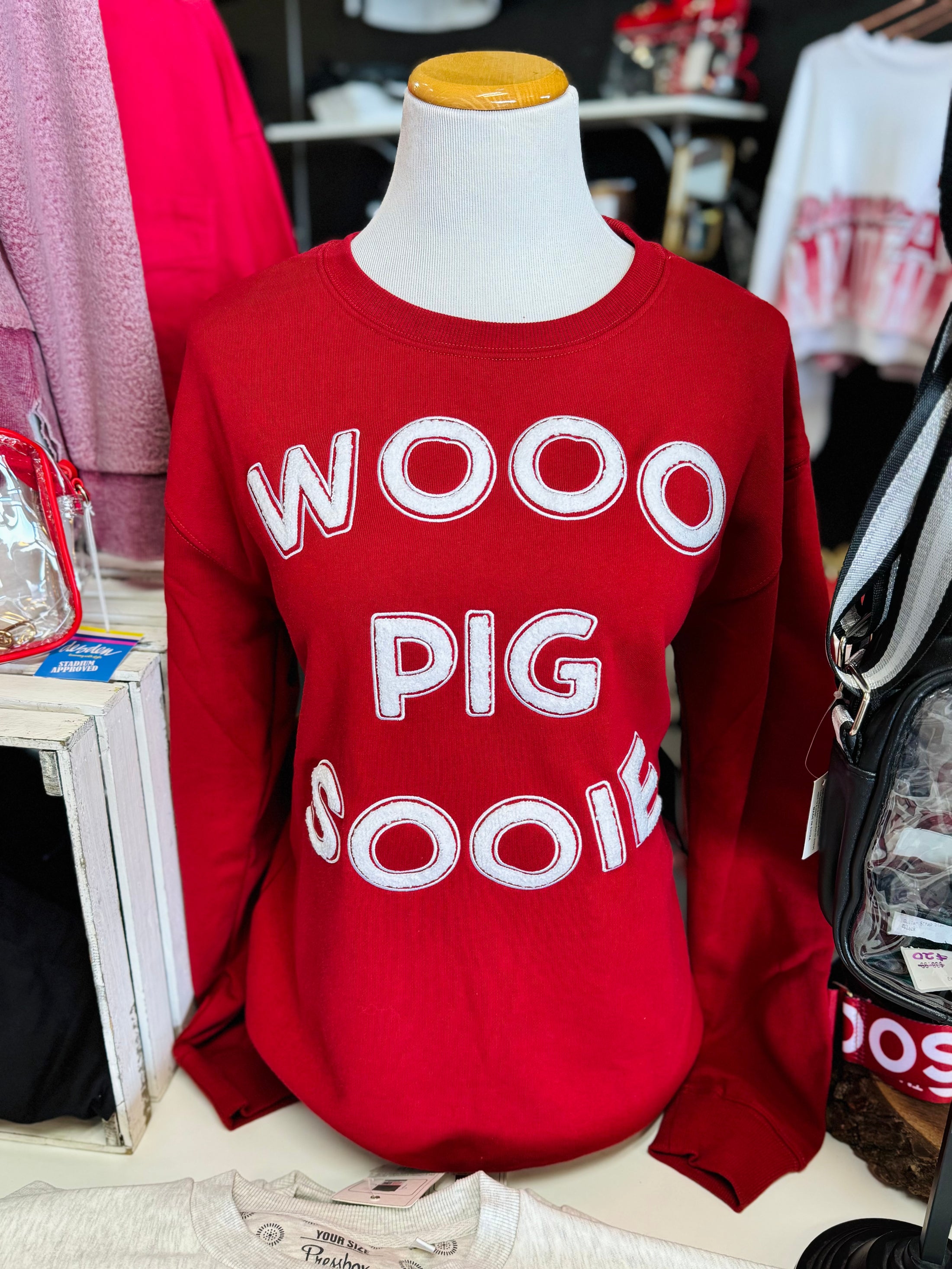 The red Wooo Pig Sooie sweatshirt with white chenille lettering displayed on a mannequin inside Whimsy Whoo, your premier Arkansas Razorback store destination.