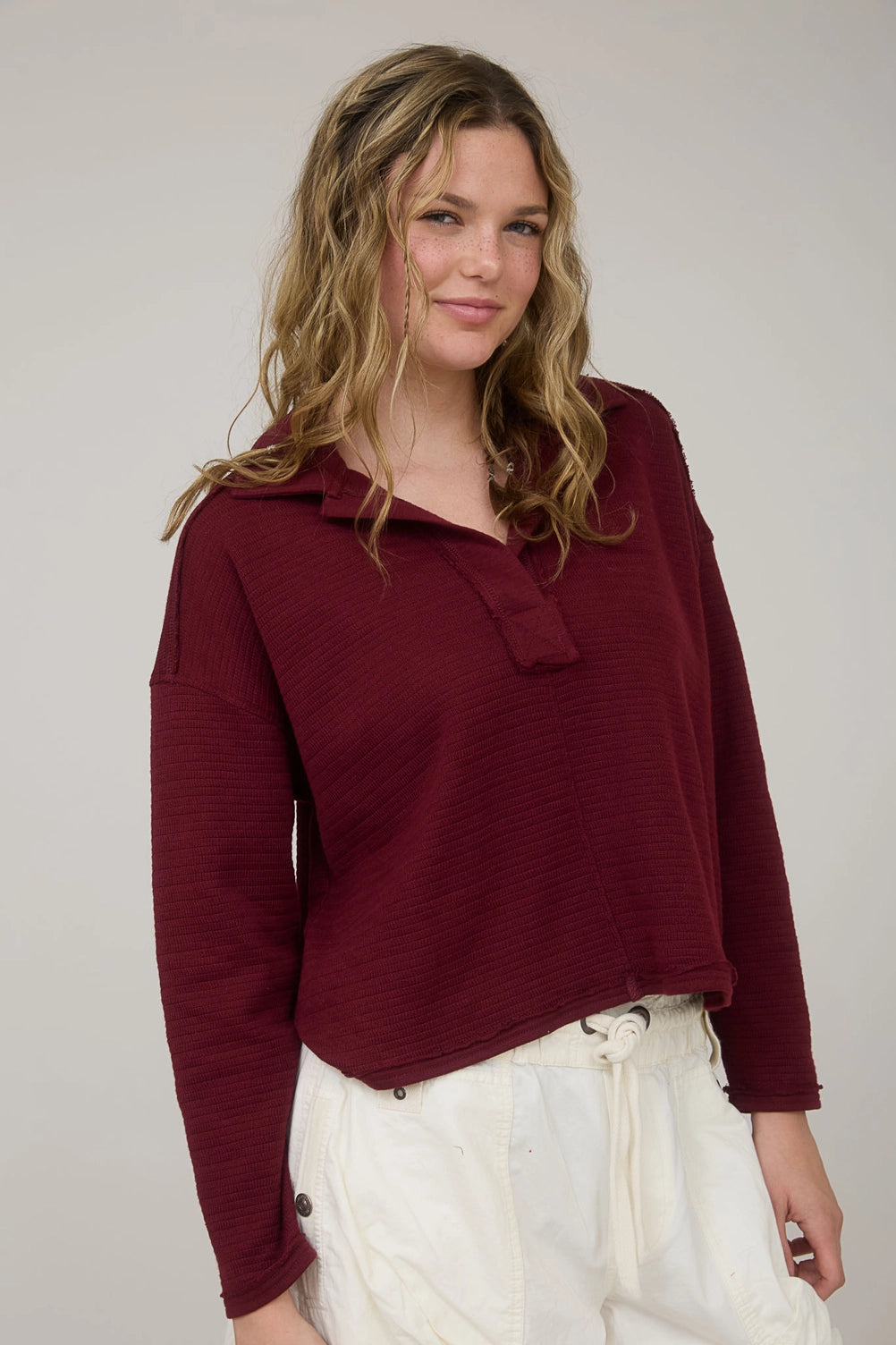 A woman wearing the Burgundy Comfy-Classic Ribbed Polo from Whimsy Boutique, a premier Arkansas boutique. This long sleeve textured knit features a relaxed fit and raw-edge hem, perfect for those looking for a boutique in Fayetteville.