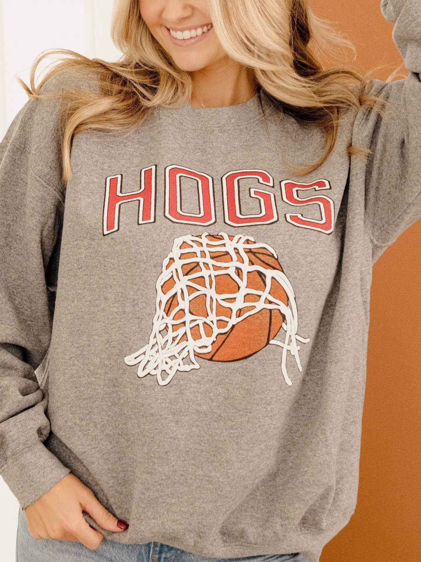 A woman smiling in the Nothing But Net Hogs Sweatshirt. This soft 50/50 cotton-poly blend crewneck is a must-have for the Arkansas basketball season.