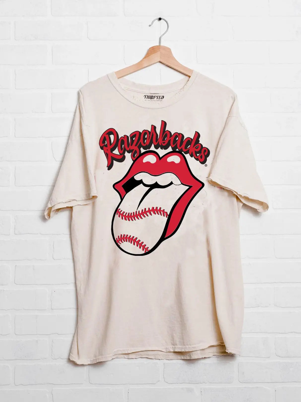 A cream-colored, 100% cotton vintage-inspired graphic tee featuring "Razorbacks" script and a rock-and-roll lip graphic with a baseball tongue. This meaningfully distressed, officially licensed tee is a retired bestseller at Whimsy Boutique in Fayetteville.
