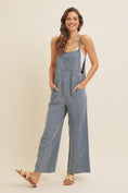 Load image into Gallery viewer, Woman wearing a blue linen-blend jumpsuit on a beige background 
