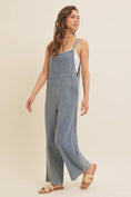 Load image into Gallery viewer, Woman wearing a blue linen-blend jumpsuit on a beige background
