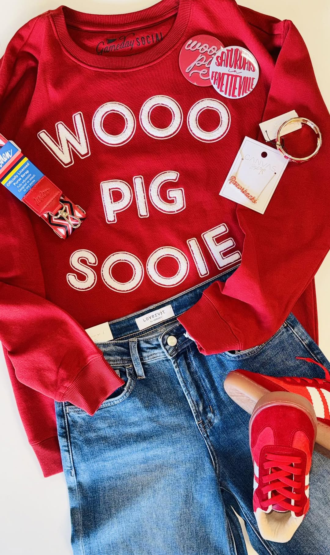 A styled gameday flat lay from Whimsy Whoo Boutique featuring the red Wooo Pig Sooie sweatshirt, Razorback jewelry, red sneakers in FAyetteville  with white chenille letters, paired with denim jeans and Arkansas Razorback  accessories.