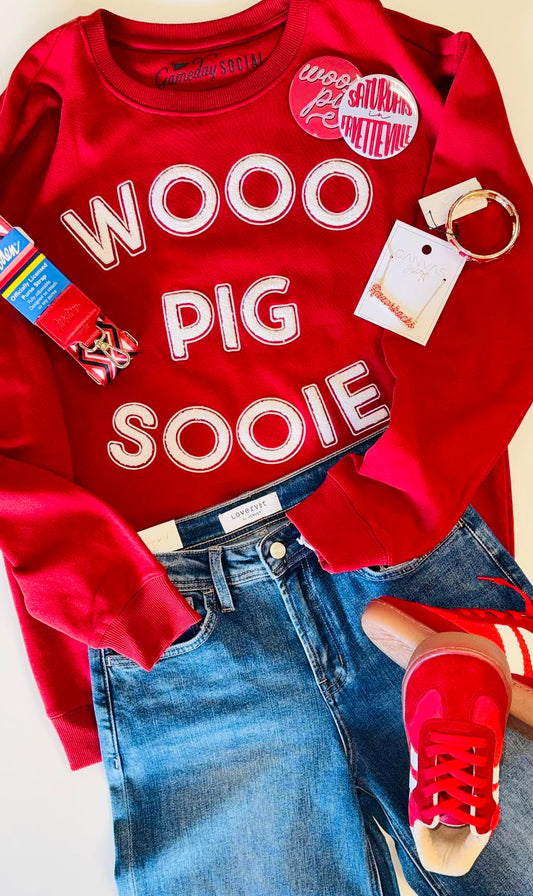 A styled gameday flat lay from Whimsy Whoo Boutique featuring the red Wooo Pig Sooie sweatshirt, Razorback jewelry, red sneakers in FAyetteville  with white chenille letters, paired with denim jeans and Arkansas Razorback  accessories.