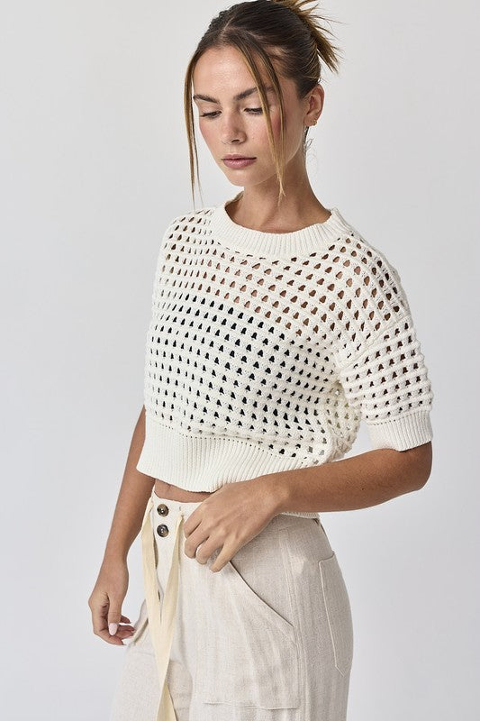 Front view of the Oh Hey Crochet! open-knit cropped sweater in white, styled with wide-leg utility pants at Whimsy Whoo Boutique.
